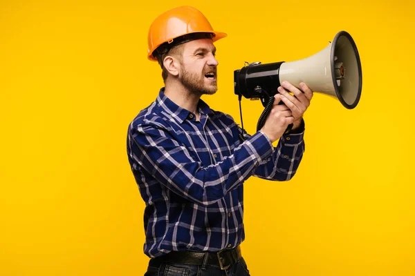 Dühös munkás ember egy megafon, sárga háttér — Stock Fotó