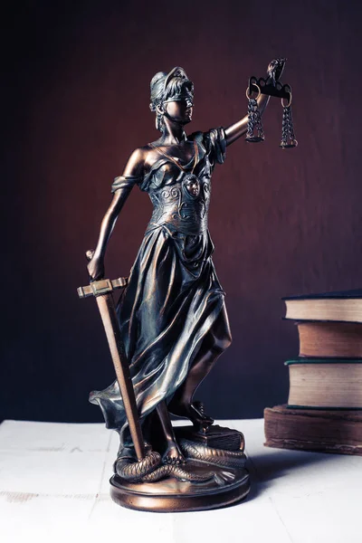 Beyaz ahşap bir masa yanında bir yığın üzerinde Themis heykelcik duruyor eski kitaplar.