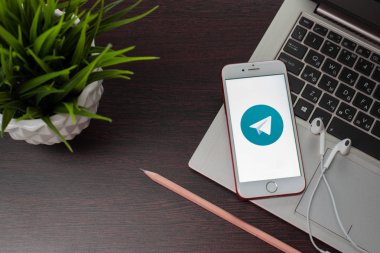 Uyandığımda üzerinde Telegram uygulaması ile Apple iPhone 8 ofiste EarPods yanında dizüstü klavye yerleştirilir