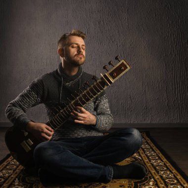 Portrait of a European man playing the sitar sitting on the carpet clipart