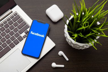 iphone X ekranındaki Facebook logosu Airpods'un yanındaki dizüstü bilgisayar klavyesine yerleştirilir.