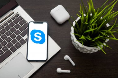 iphone X ekranındaki Skype logosu Airpods'un yanındaki dizüstü bilgisayar klavyesine yerleştirilir.