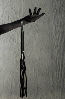 Elinde kırbaç tutan saten eldivenli bir kadın eli. Bdsm kıyafeti