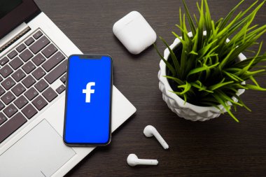 iphone X ekranındaki Facebook logosu Airpods'un yanındaki dizüstü bilgisayar klavyesine yerleştirilir.