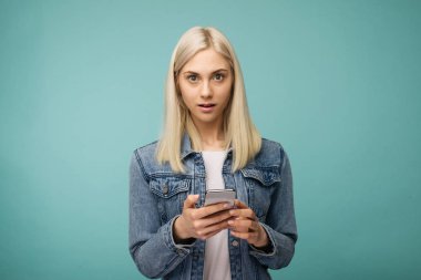 Genç, güzel, şaşkın bir kadın akıllı telefon kullanıyor..