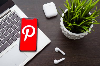 iphone X ekranındaki Pinterest logosu Airpods'un yanındaki dizüstü bilgisayar klavyesine yerleştirilir.