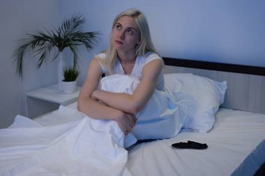 Uyku bozuklukları, uykusuzluk. Yatakta pijamalarıyla oturan Depresyondan muzdarip Kadın