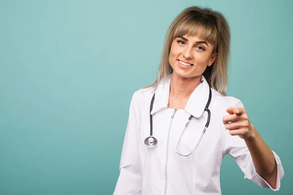 Gülümseyen genç kadın doktor parmaklarıyla kameraya bir stetoskop ile işaret — Stok fotoğraf