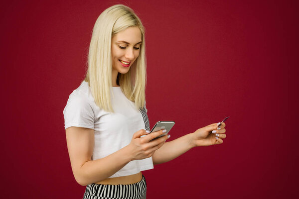 Young smiling woman buys online. Holds a smartphone and a credit card in hand