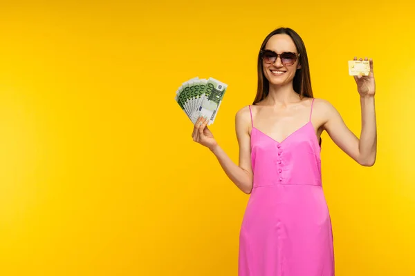 100ユーロ紙幣とクレジットカードを保持するピンクのドレスとサングラスを着たスレンダースペインの女の子 — ストック写真