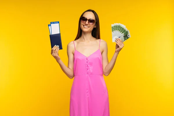 ピンクのドレスとサングラスを着たスレンダーな女の子は、航空券と100ユーロ紙幣でパスポートを保持 — ストック写真
