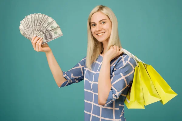 Lycklig tjej i en rutig blus rymmer 100 dollar räkningar och shoppingväskor — Stockfoto