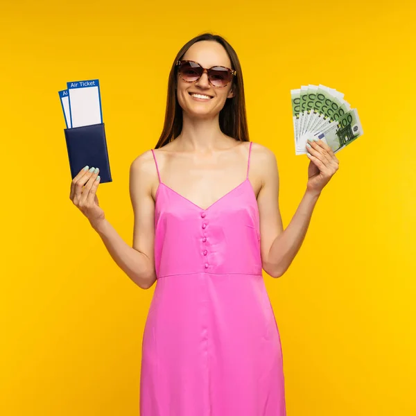 ピンクのドレスとサングラスを着たスレンダーな女の子は、航空券と100ユーロ紙幣でパスポートを保持 — ストック写真