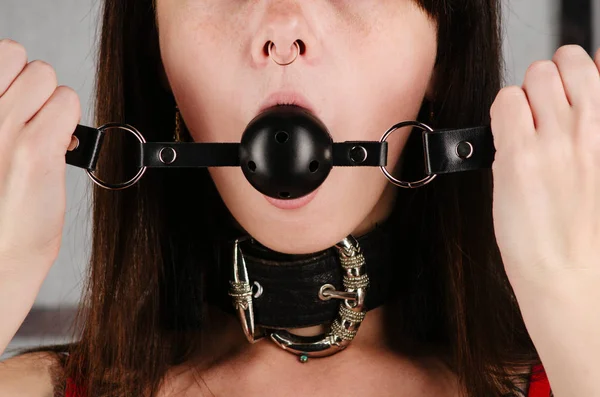 BDSM outfit for adult sex games. A young woman with a collar holds a gag in her mouth. — Stock Photo, Image