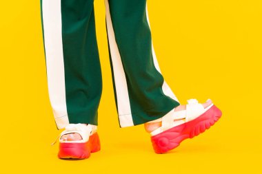 Kırmızı tabanlı spor sandaletlerde kadın bacakları ve çizgili yeşil pantolon