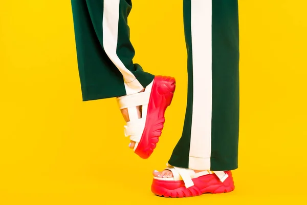 Pernas femininas em sandálias esportivas com sola vermelha e calças verdes sagacidade — Fotografia de Stock