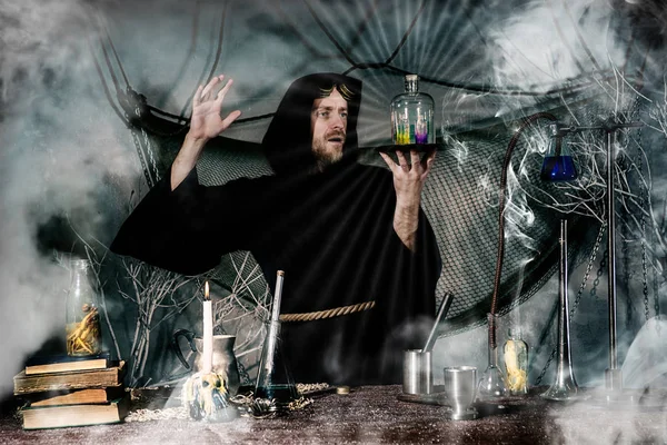 The medieval alchemist make magic ritual at the table in his smoke laboratory. — Stock Photo, Image