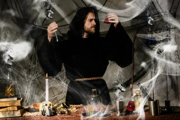 The medieval alchemist make magic ritual at the table in his smoke laboratory. — Stock Photo, Image