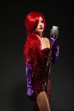 Genç Kızıl saçlı kadın retro tarzı şarkıcı. Vintage mikrofon ve koyu arka plan