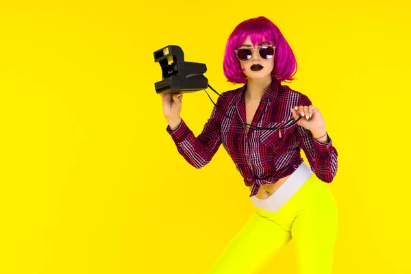 Retrato de chica de moda con cámara sobre fondo amarillo. Mujer joven de estilo loco en peluca rosa — Foto de Stock