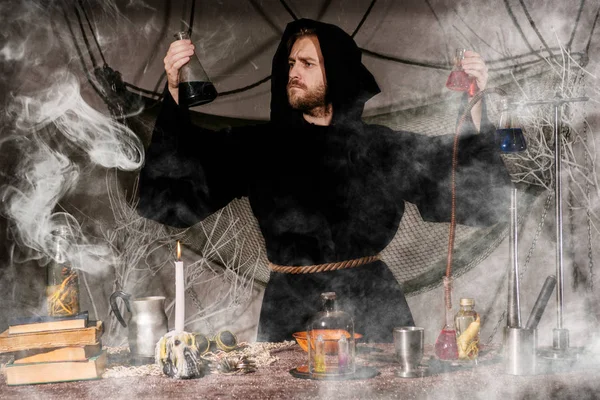 The medieval alchemist make magic ritual at the table in his smoke laboratory. — Stock Photo, Image