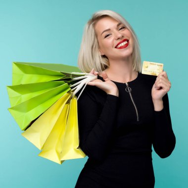 Güzel bir mutlu genç sarışın kadın alışveriş çantaları tutarak mavi duvar arka plan üzerinde izole poz Görüntü.