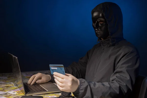 Anonieme hacker in Mask programmeur maakt gebruik van een laptop om het systeem te hacken in het donker. — Stockfoto
