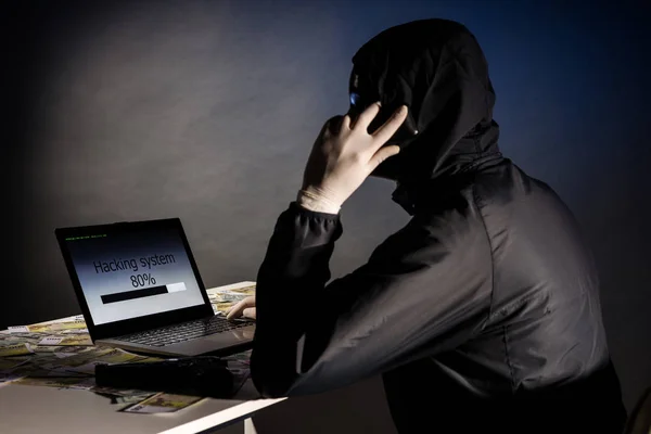 Ein anonymer Hacker mit Maske sitzt seitlich mit einem Laptop und telefoniert, um das System im Dunkeln zu hacken. das Konzept der Cyberkriminalität und Hacking-Datenbank — Stockfoto