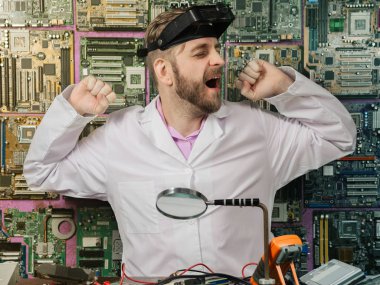 Genç erkek elektrikçi mühendis, elektrik laboratuvarının masasında otururken yorgun bir şekilde esneme