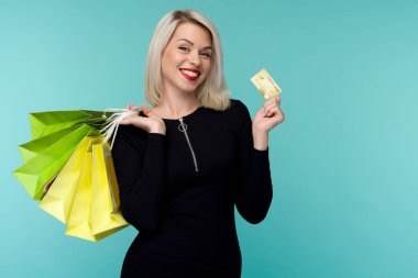 Güzel bir mutlu genç sarışın kadın alışveriş çantaları tutarak mavi duvar arka plan üzerinde izole poz Görüntü.