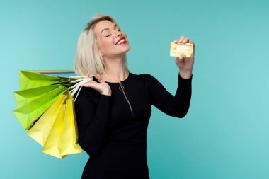 Güzel bir mutlu genç sarışın kadın alışveriş çantaları tutarak mavi duvar arka plan üzerinde izole poz Görüntü.