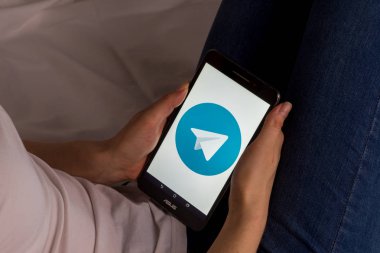 Tula, Rusya, 17 Eylül 2019: Asyalı kız yatakta yatıyor ve ekranda Telegram logosu olan bir tablet tutuyor.