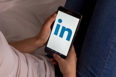 Tula, Rusya, 17 Eylül 2019: Asyalı kız yatakta yatıyor ve ekranda Linkedin logolu bir tablet tutuyor.