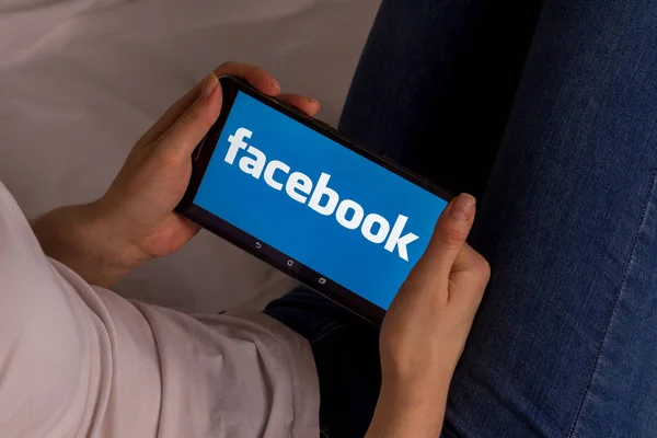 Tula, Rusia, 17 de septiembre de 2019: Chica asiática se acuesta en la cama y sostiene una tableta con el logotipo de Facebook en la pantalla . — Foto de Stock