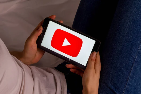 Tula, Rusia, 17 de septiembre de 2019: Chica asiática se acuesta en la cama y sostiene una tableta con el logotipo de Youtube en la pantalla . — Foto de Stock