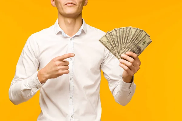 Joyful Asian man i en vit skjorta pekar ett finger på pengar dollar på en gul bakgrund — Stockfoto