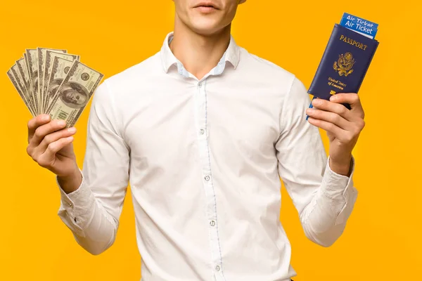En snygg asiatisk man i en vit skjorta gläds åt att vinna lotteriet. Han håller ett pass med flygbiljetter och pengar dollar på en gul bakgrund. — Stockfoto