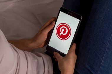 Tula, Rusya, 17 Eylül 2019: Asyalı kız yatakta yatıyor ve ekranda Pinterest logolu bir tablet tutuyor.