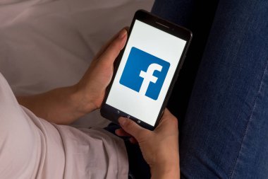 Tula, Rusya, 17 Eylül 2019: Asyalı kız yatakta yatıyor ve ekranda Facebook logosu olan bir tablet tutuyor.