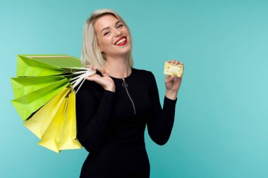 Güzel bir mutlu genç sarışın kadın alışveriş çantaları tutarak mavi duvar arka plan üzerinde izole poz Görüntü.