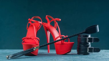 Yetişkin seks oyunları için Bdsm kıyafeti. Kırmızı yüksek topuklu striptiz ayakkabı ve kelepçe, koyu arka plan üzerinde kırbaç