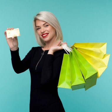 Güzel bir mutlu genç sarışın kadın alışveriş çantaları tutarak mavi duvar arka plan üzerinde izole poz Görüntü.