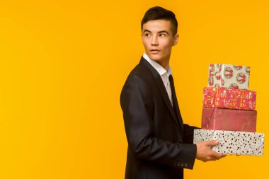 Yakışıklı asyalı işadamı sarı arka plan üzerinde hediye kutusu tutan