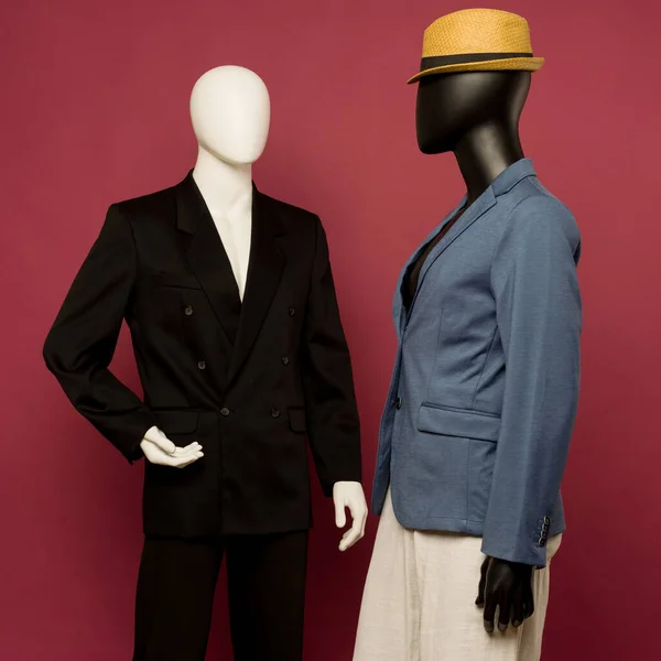 Two male mannequin in a black business suit and in a blue suit and white pants on a ruby background - image