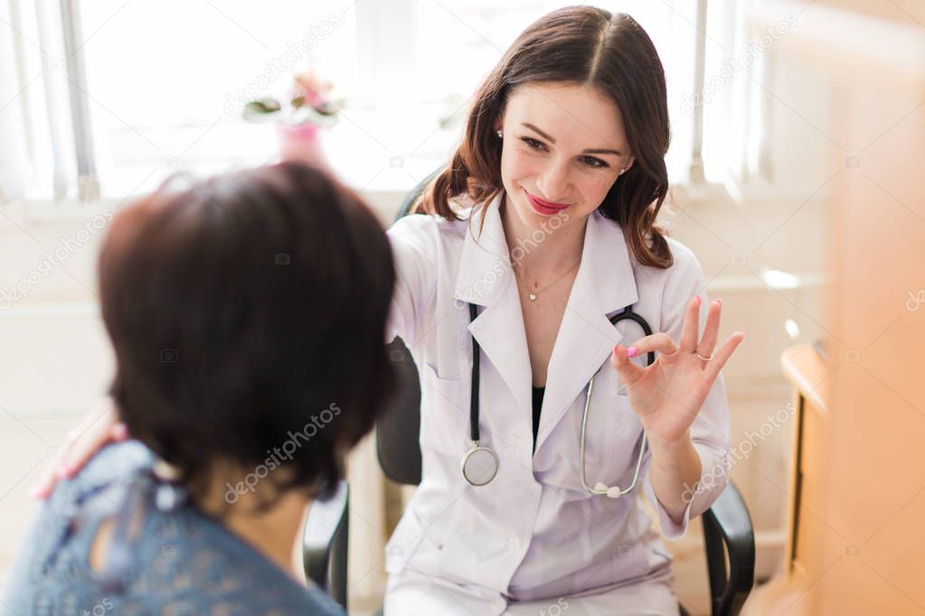 The young cheerful breast specialist talking with the patient in her office and showing a gesture