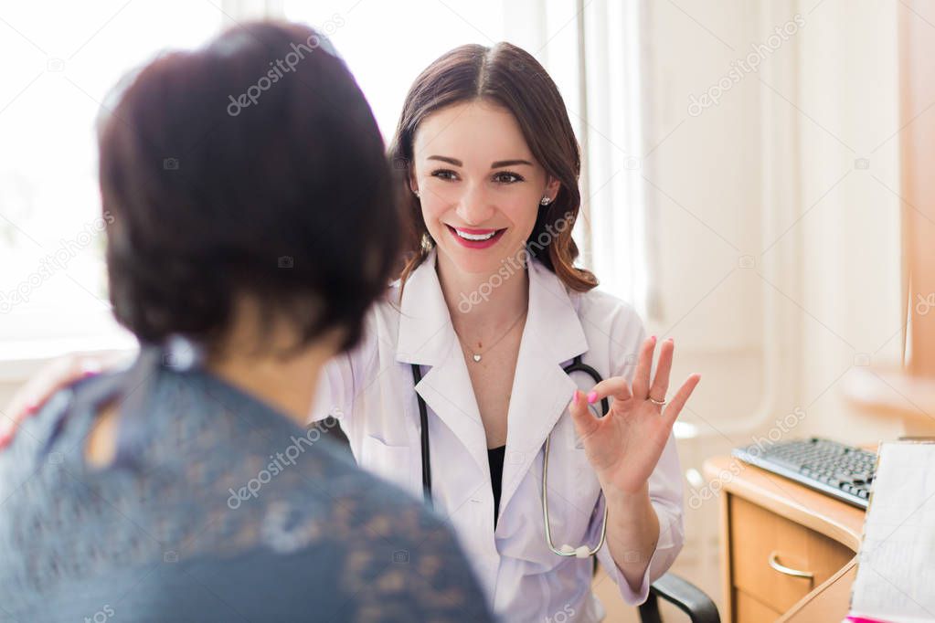 The young smiling breast specialist talking with the patient in her office and showing a gesture
