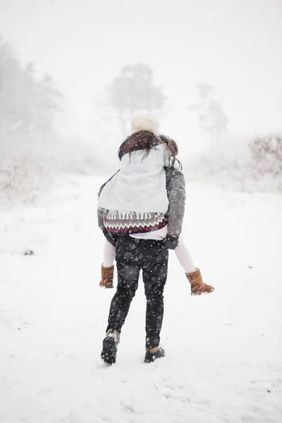 雪に覆われた公園の彼の女性の背部で保持している若い男の背面図 — ストック写真