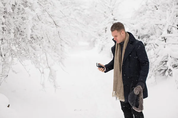 英俊的年轻人站在白雪覆盖的公园里 拿着电话 — 图库照片