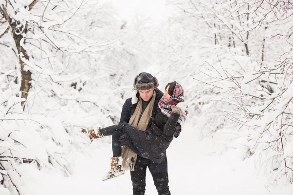 在白雪覆盖的公园里抱着年轻微笑的美丽女人的快乐年轻人 — 图库照片