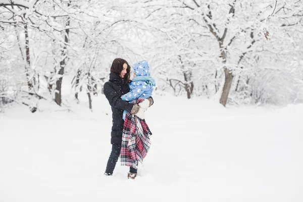 快乐的年轻母亲站在白雪覆盖的公园 抱着她可爱的小儿子在怀里 — 图库照片
